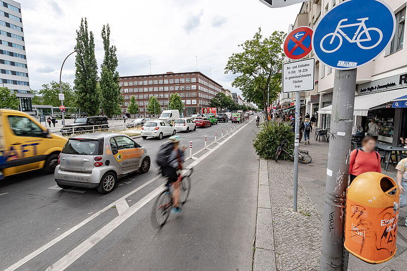 geschützter Radfahrstreifen am rechten Fahrbahnrand, daneben zwei Fahrspuren, auf einer belebten Geschäftsstraße