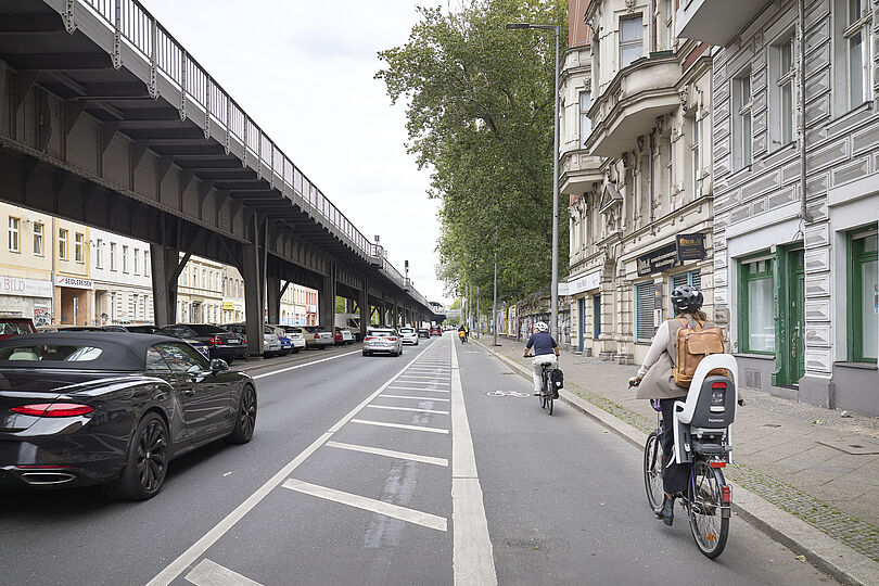 Radfahrstreifen mit Fahrradpiktogrammen, Sicherheitstrennstreifen und Radfahrenden.