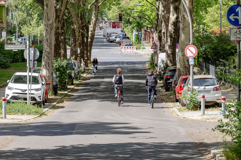 Fahrradfahrer fahren auf einer Stadtstraße auf eine Ampel zu, links und rechts parkende Autos