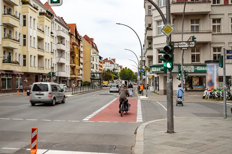 Kreuzung Grunewaldstraße/Eisenacher Straße mit rotmarkiertem Radfahrstreifen, auf dem ein Fahrradfahrer fährt. Grüne Ampel im Vordergrund.