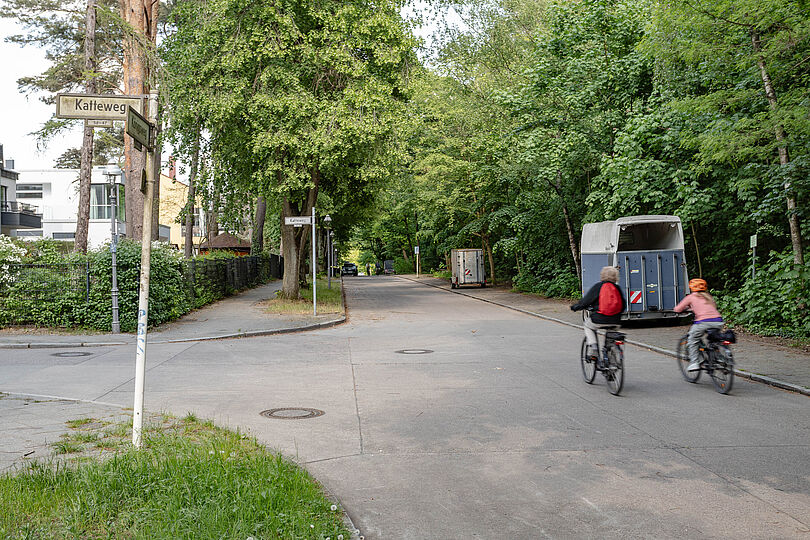 Fahrradfahrer fahren nebeneinander auf einer Wohnstraße, an deren Rand Anhänger parken