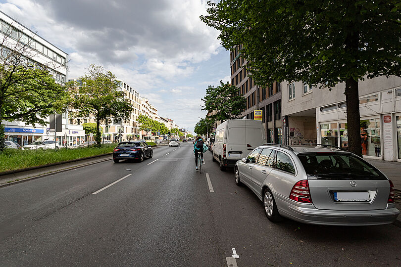 Blick auf die Müllerstraße ohne Infrastruktur für Radfahrende, parkende Autos am rechten Fahrbahnrand