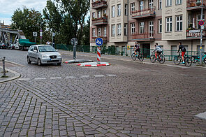 Fahrradfahrende nutzen einen engen Radweg. Im Vordergrund sieht man das Kopfsteinpflaster der Swinemünder Straße.