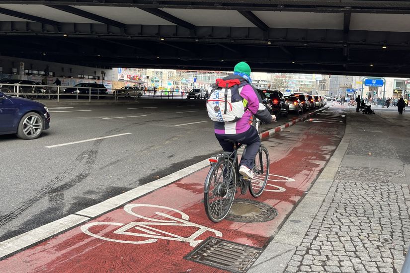 Radfahrende auf einem rotbeschichten Radfahrstreifen. Der Radfahrstreifen ist mit rotweiß markierten Trennelementen vom Autoverkehr getrennt.