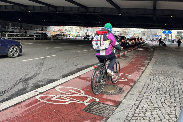 Radfahrende auf einem rotbeschichten Radfahrstreifen. Der Radfahrstreifen ist mit rotweiß markierten Trennelementen vom Autoverkehr getrennt.