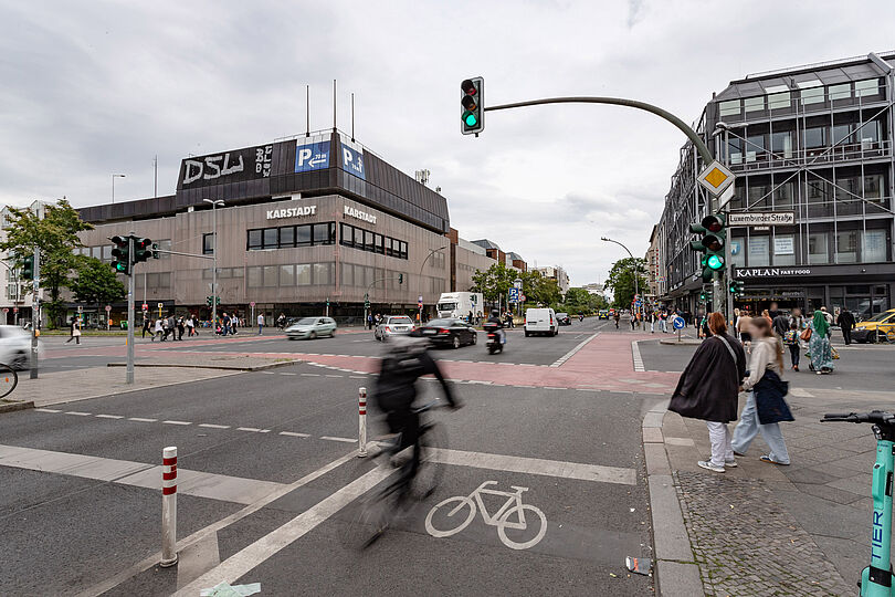 geschützter Radfahrstreifen am rechten Fahrbahnrand vor einer Kreuzung mit rotmarkierten Schutzstreifen für den Radverkehr, belebte Geschäftsstraße