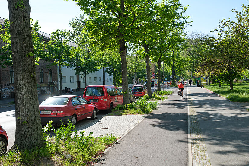 breiter grauer Radweg zwischen Gehweg und parkenden Autos auf der Straße