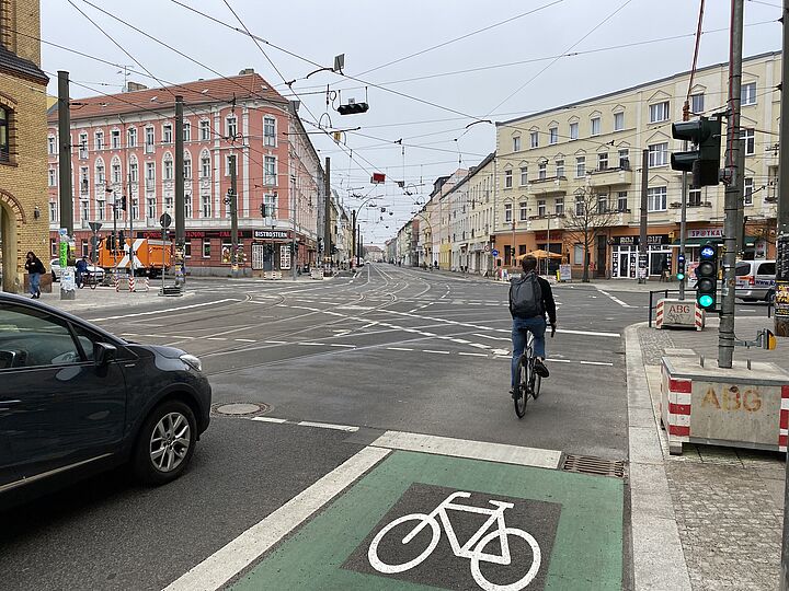 Grünmarkierter Schutzstreifen mit einem Piktogramm auf einem großen Kreuzungsbereich mit einem Fahrradampel.