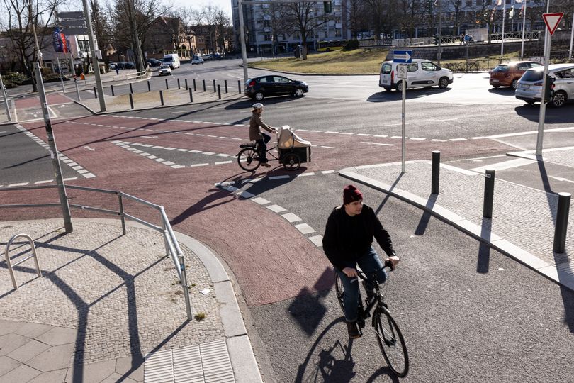 Ein Lastenfahrrad überquert eine rotmarkierte Kreuzung, ein Fahrradfahrer biegt an der Kreuzung ab