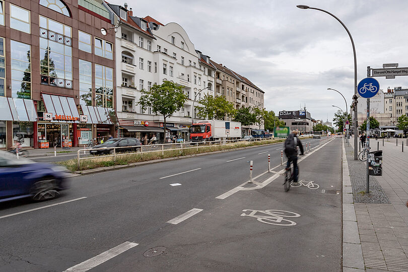 geschützter Radfahrstreifen am rechten Fahrbahnrand, daneben zwei Fahrspuren, auf einer belebten Geschäftsstraße