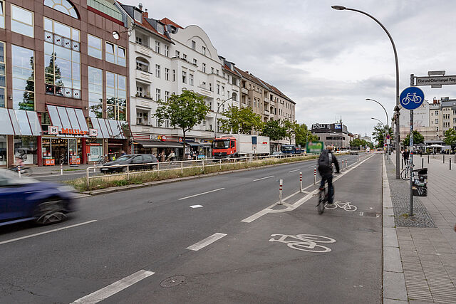 geschützter Radfahrstreifen am rechten Fahrbahnrand, daneben zwei Fahrspuren, auf einer belebten Geschäftsstraße