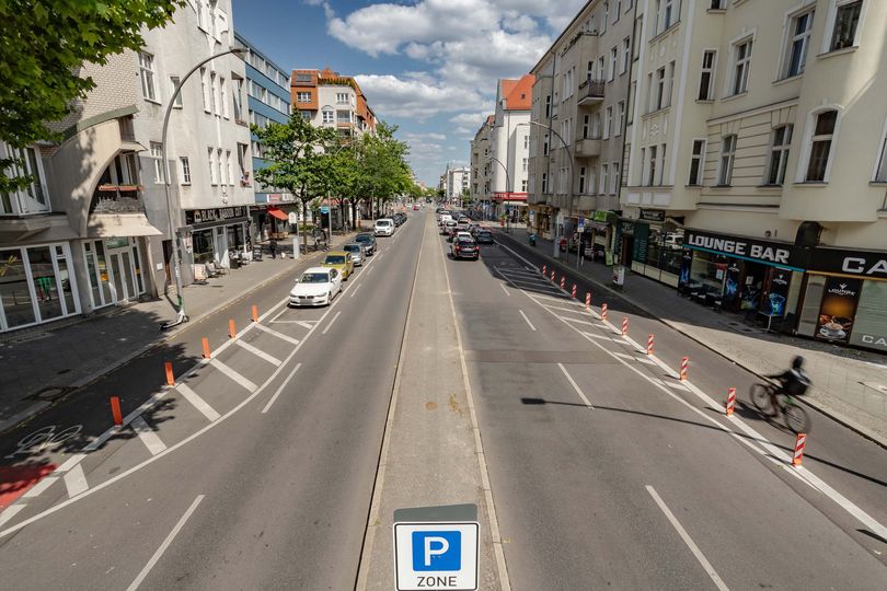 Blick auf eine Stadtstraße mit zwei Fahrbahnen, Mittelstreifen, markierten Parkplätzen und Lieferzonen sowie geschützten Radfahrstreifen
