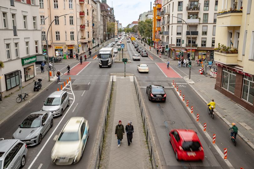 Blick aus der Vogelperspektive auf die Grunewaldstraße mit Mittelstreifen, Fahrspuren für Autoverkehr, markierten Parkplätzen und geschützten Radfahrstreifen. Viel Auto-, Fahrrad- und Fußverkehr.