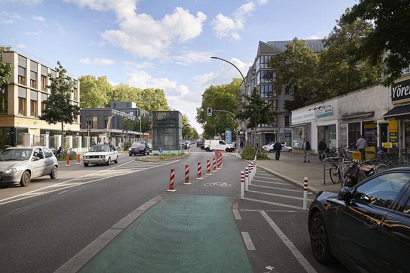 Ein grünmarkierter und teilweise mit Pollern geschützter Radweg mit einem Fahrradpiktogramm.